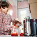 little girl making fresh strawberry and other fruit juice for breakfast