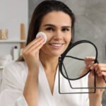 Best Reusable Makeup Remover Pads for On-the-Go Young woman cleaning her face with cotton pad near mirror in bathroom
